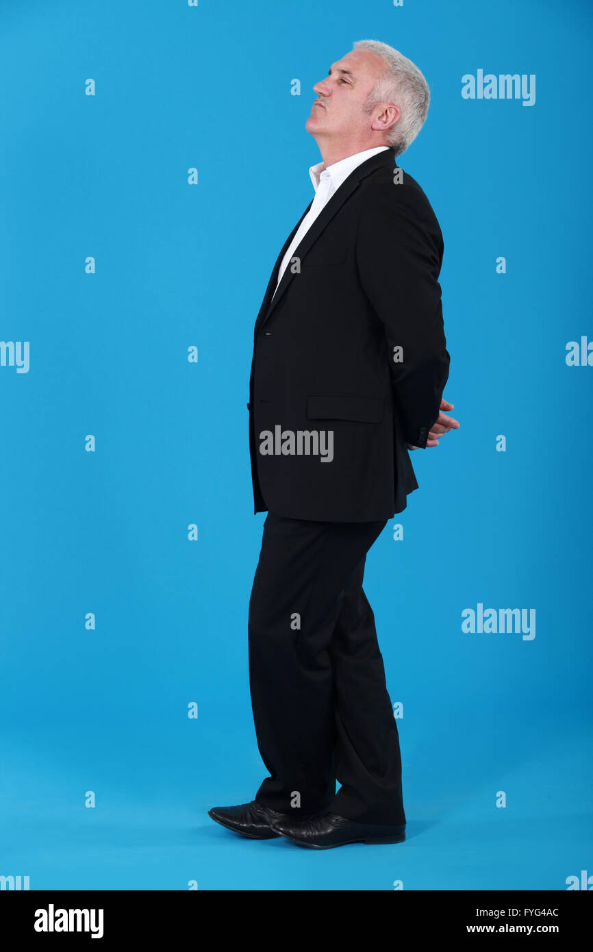 middle-aged man standing with arms behind his back isolated on blue Stock Photo