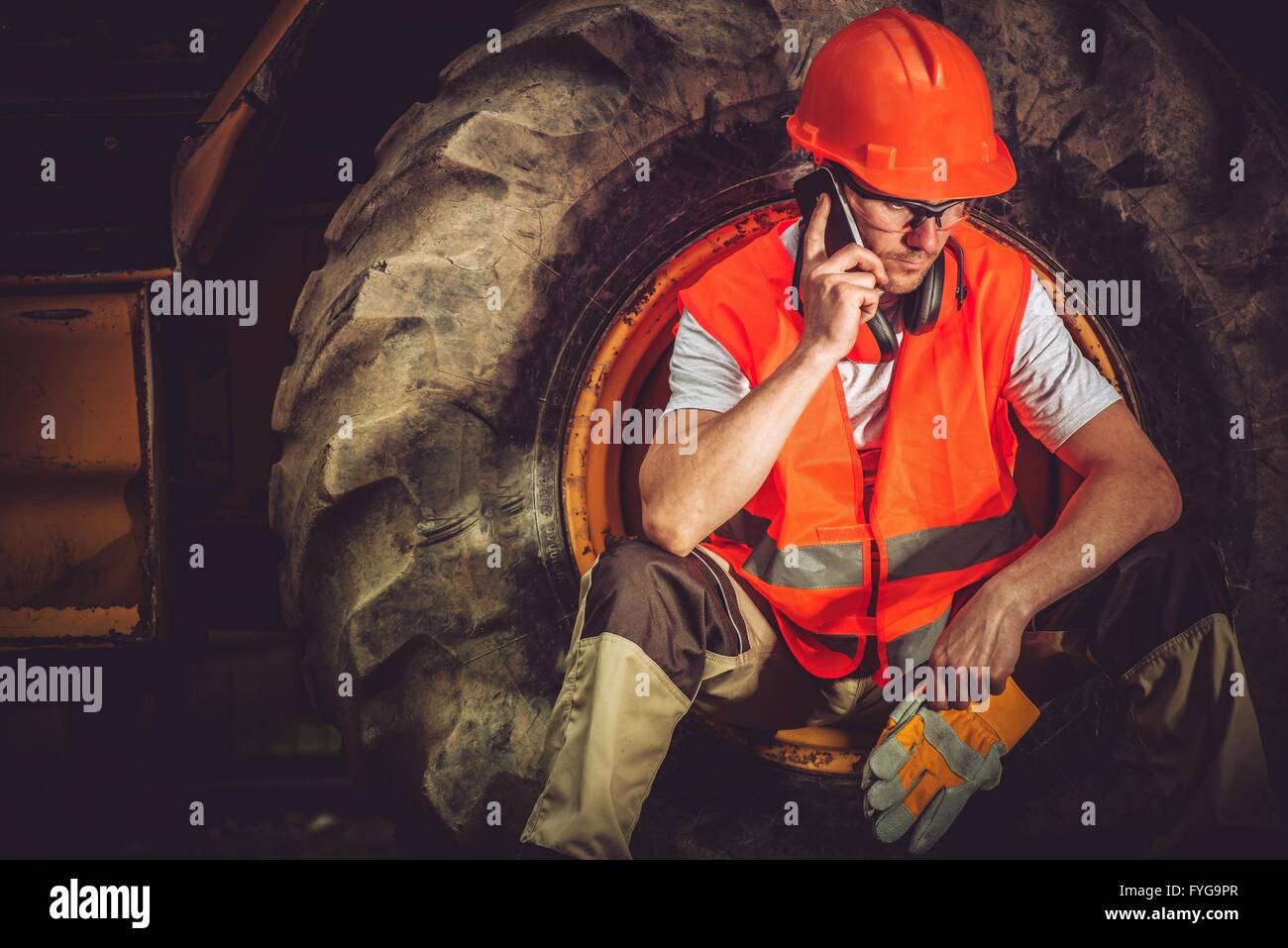 Hard Construction Business Concept with Caucasian Businessman Making Business Call While Seating Inside Heavy Duty Bulldozer Tir Stock Photo