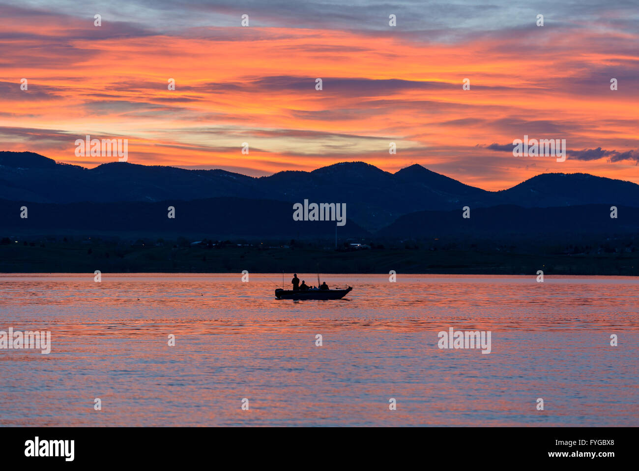 Fishing on Sunset Lake - A small fishing boat gliding cross sparkling surface of a sunset mountain lake. Stock Photo