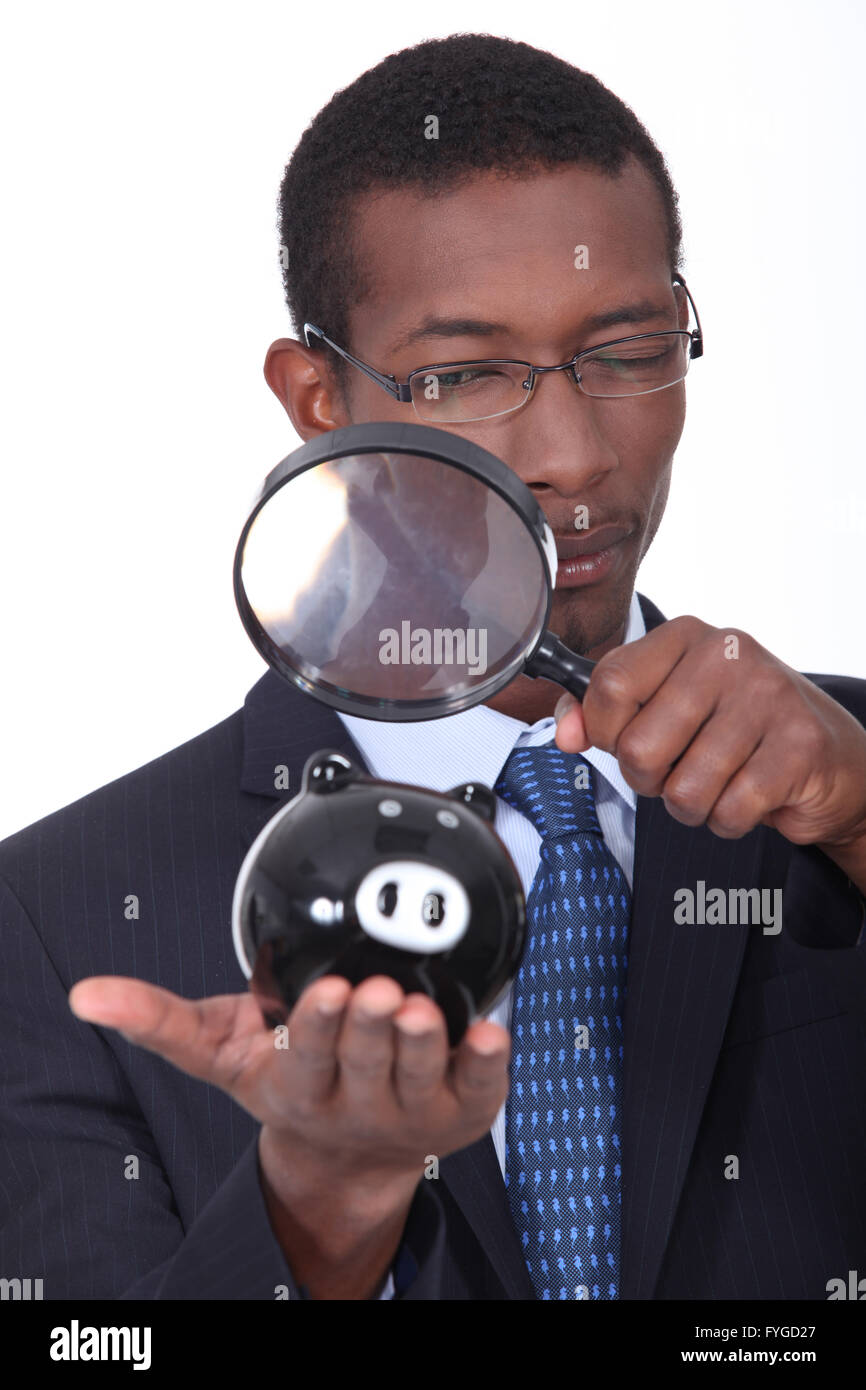 black well dressed man watching a piggy bank with a magnifying glass