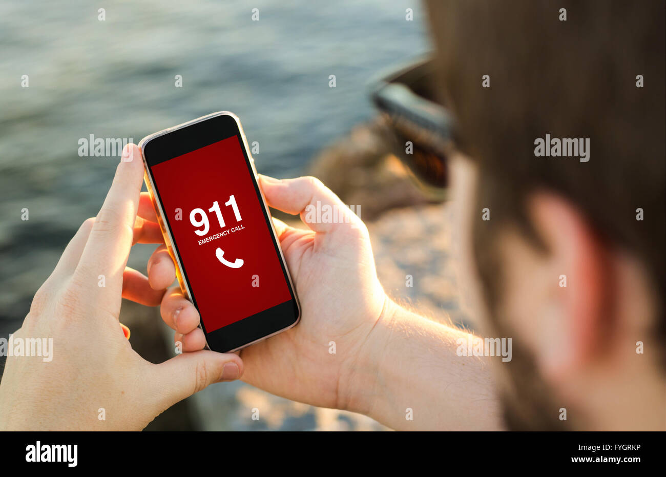 man on the coast with emergency call on his smartphone . All screen graphics are made up. Stock Photo