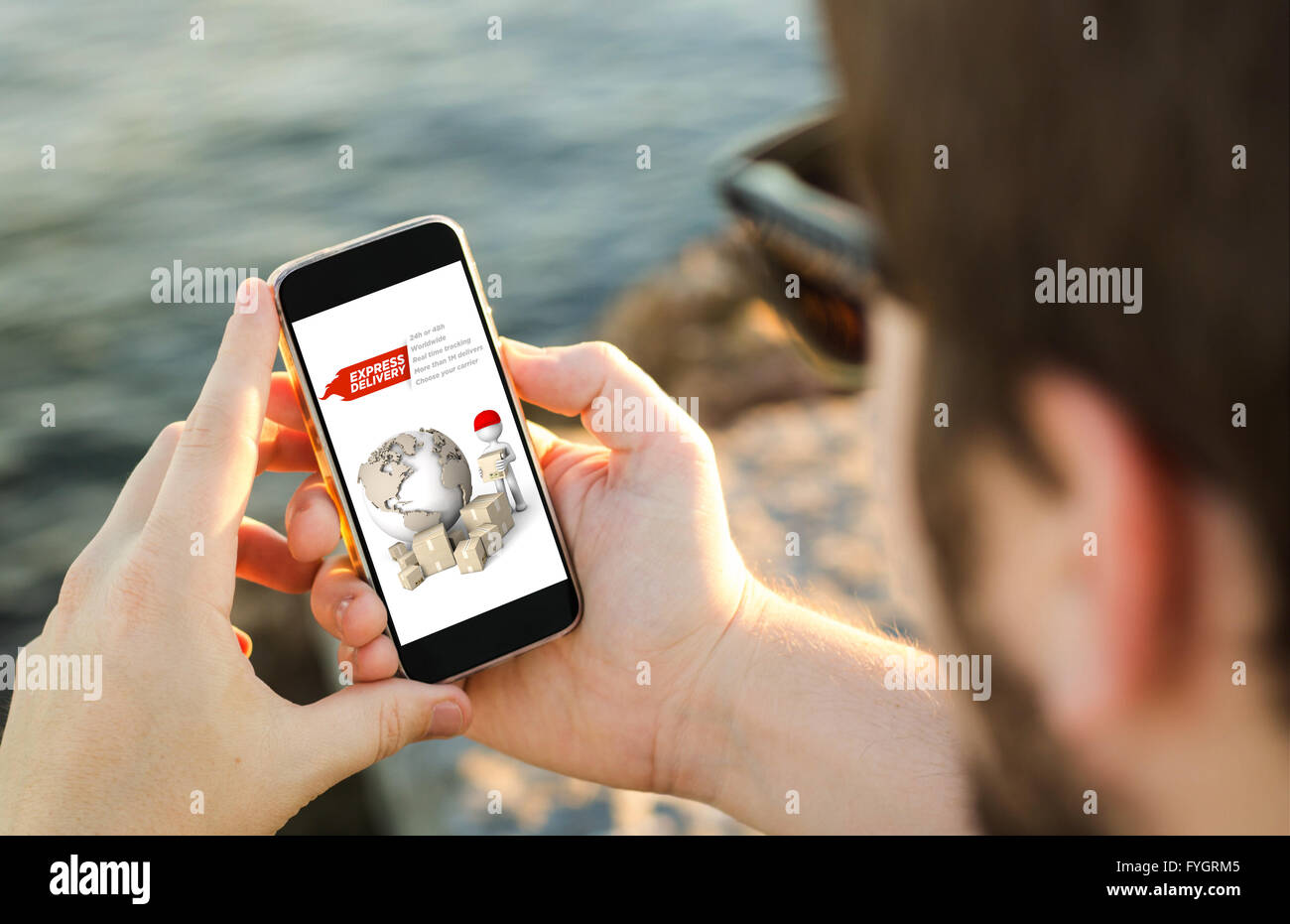 man on the coast using his smartphone showing express delivery website. All screen graphics are made up. Stock Photo
