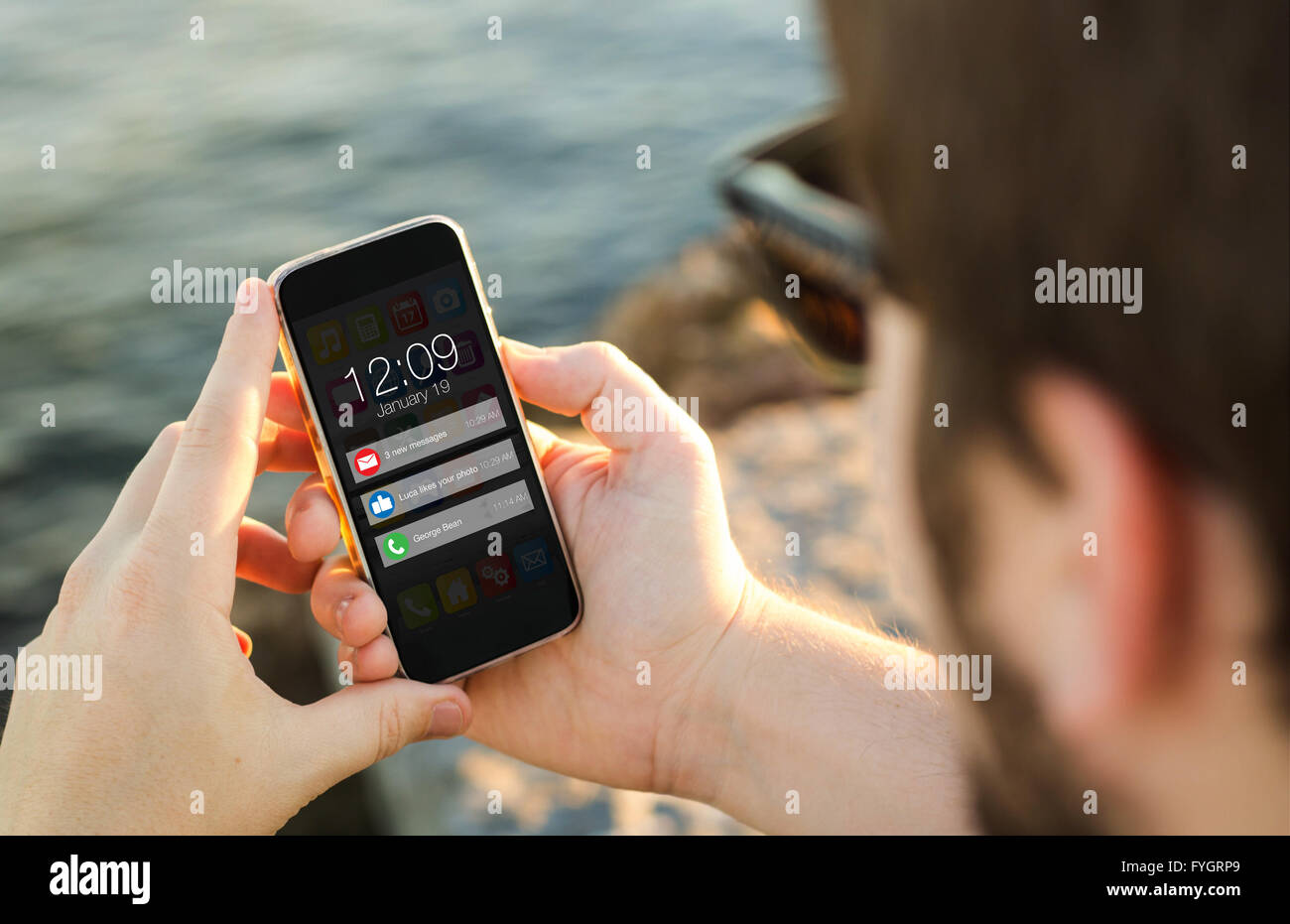 man on the coast looking at notifications on his smartphone. All screen graphics are made up. Stock Photo