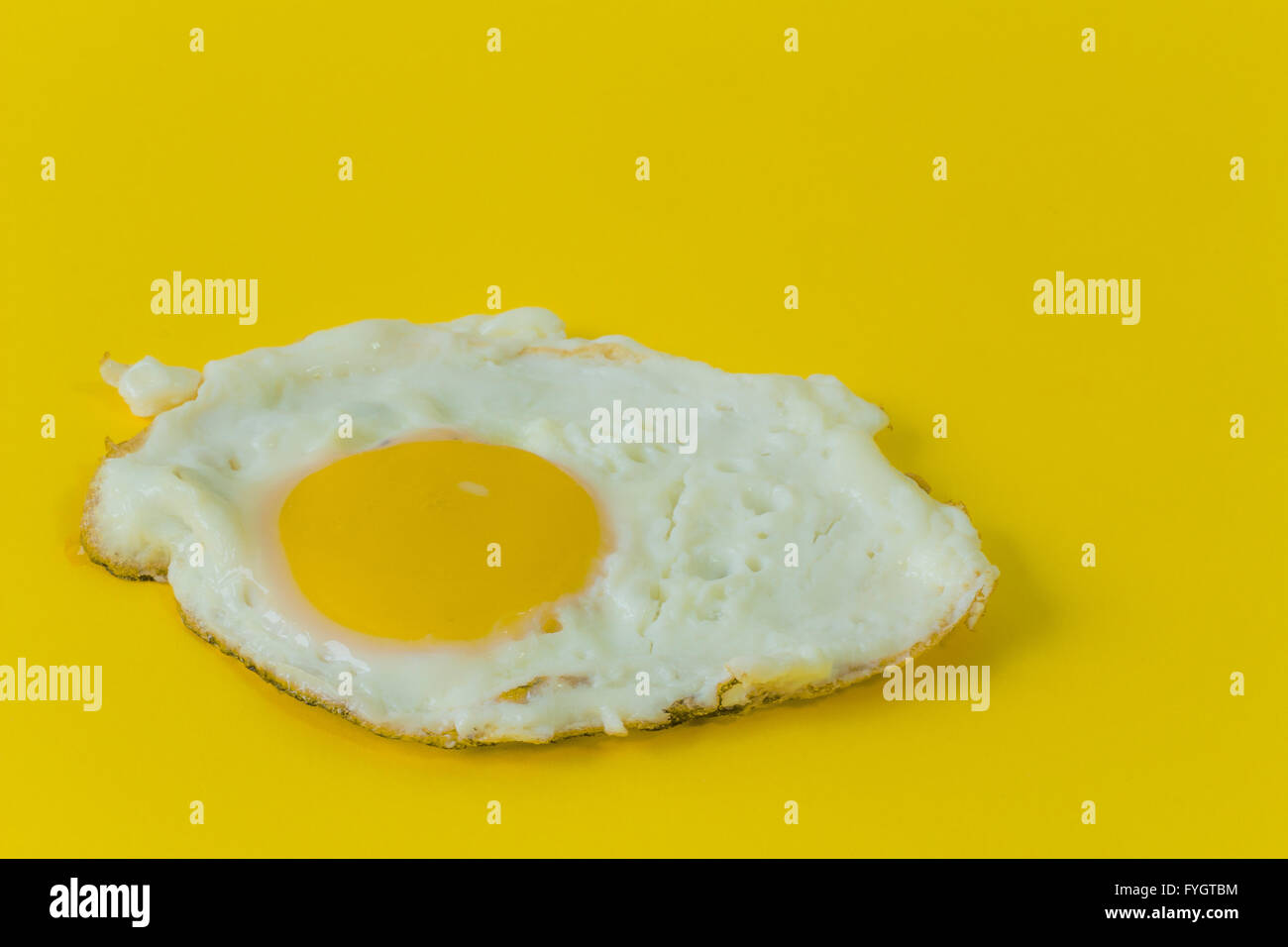 fried egg with lacy brown edges on yellow background Stock Photo