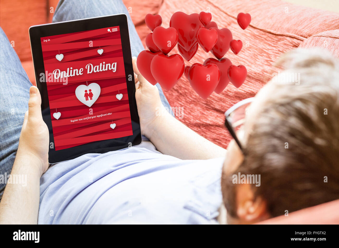 technology lifestyle love finder concept: hipster man online dating on a tablet at the sofa with love hearts in the air. Screen Stock Photo