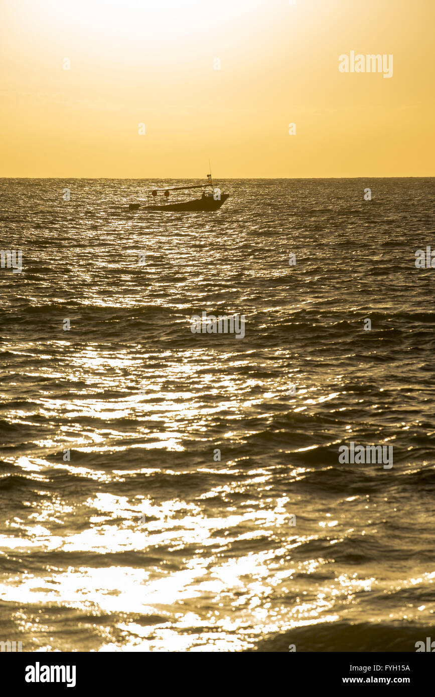 Boat sailing in the ocean at distance, sunset time on a summer day with calm sea waves. Stock Photo