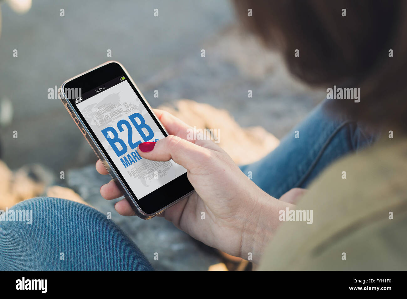 woman holding a smartphone and touching the screen shoing b2b marketing concept. All screen graphics are made up. Stock Photo