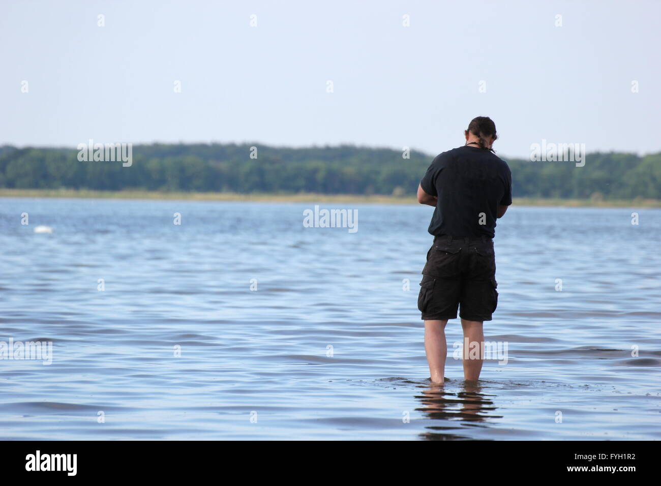Person standing in shallow water staring at the sea. Stock Photo