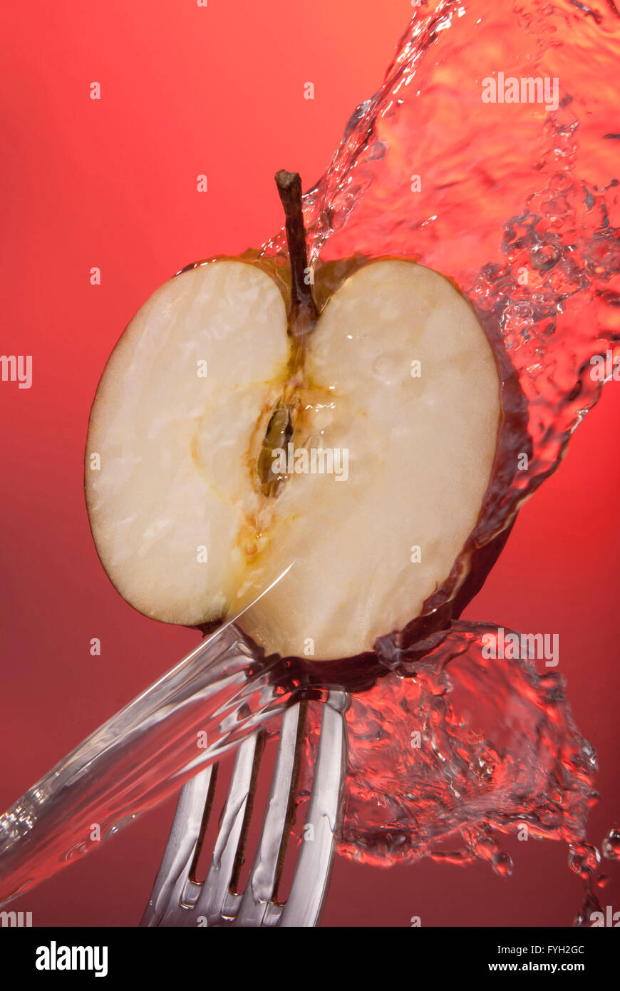 Red apple cut in half on fork with water splash, color background concept photo. Ideal for healthy eating campaign. Stock Photo