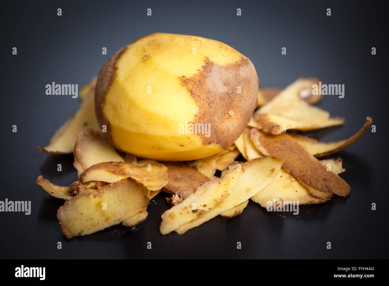 Raw peeled potatoes and potato peelings on black background Stock Photo