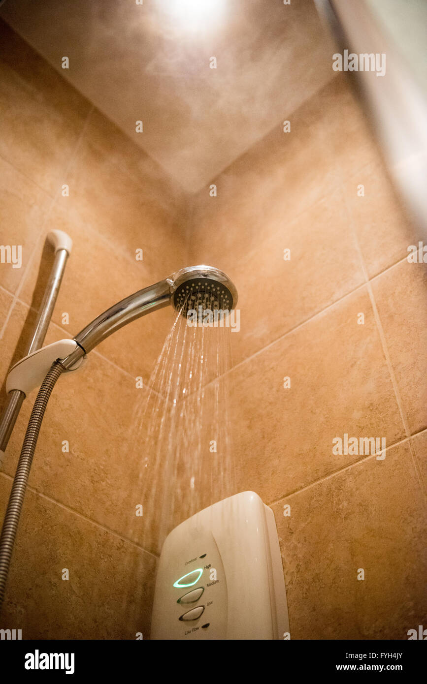 Steam and heat rising to a ceiling light from a chrome shower head in a small tiled domestic shower Stock Photo