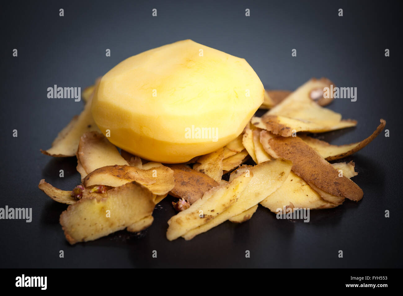 Raw peeled potatoes and potato peelings on black background Stock Photo