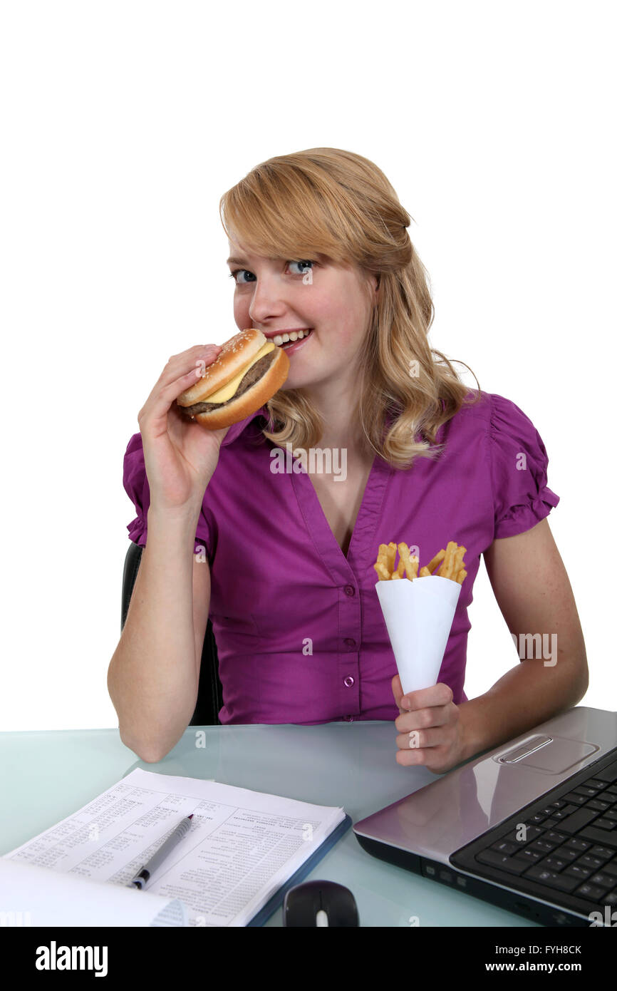 Woman eating a cheeseburger and fries at her desk Stock Photo