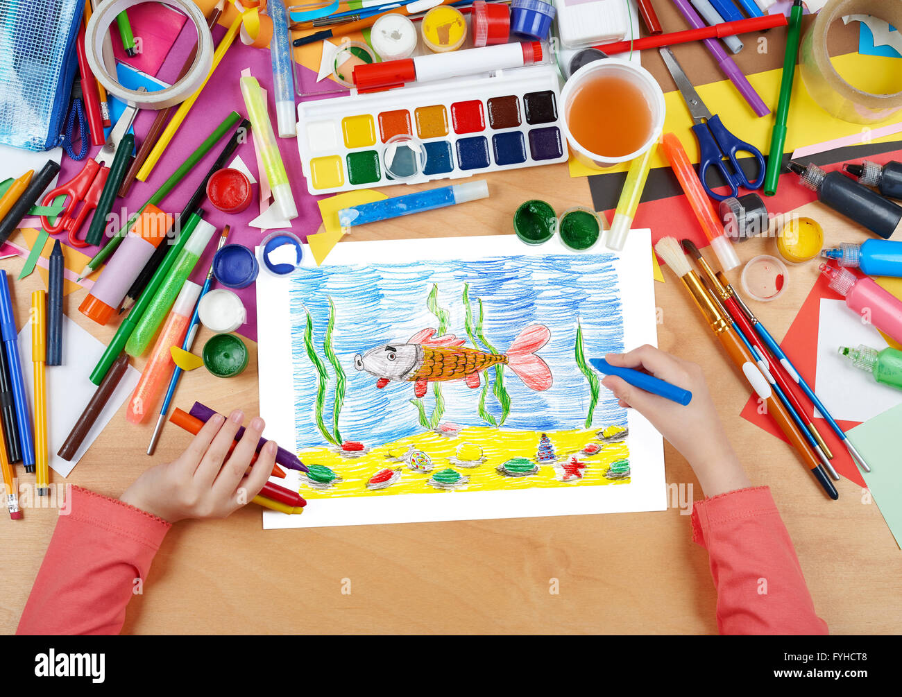 child drawing fish underwater and seabed, top view hands with pencil painting picture on paper, artwork workplace Stock Photo