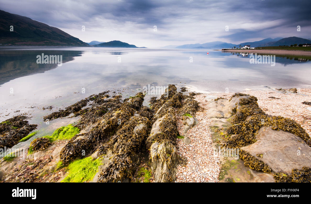 A Rocky shore and pebble beach reaches into Loch Linnhe sea loch at Onich near Glencoe in the Highlands of Scotland, with mounta Stock Photo