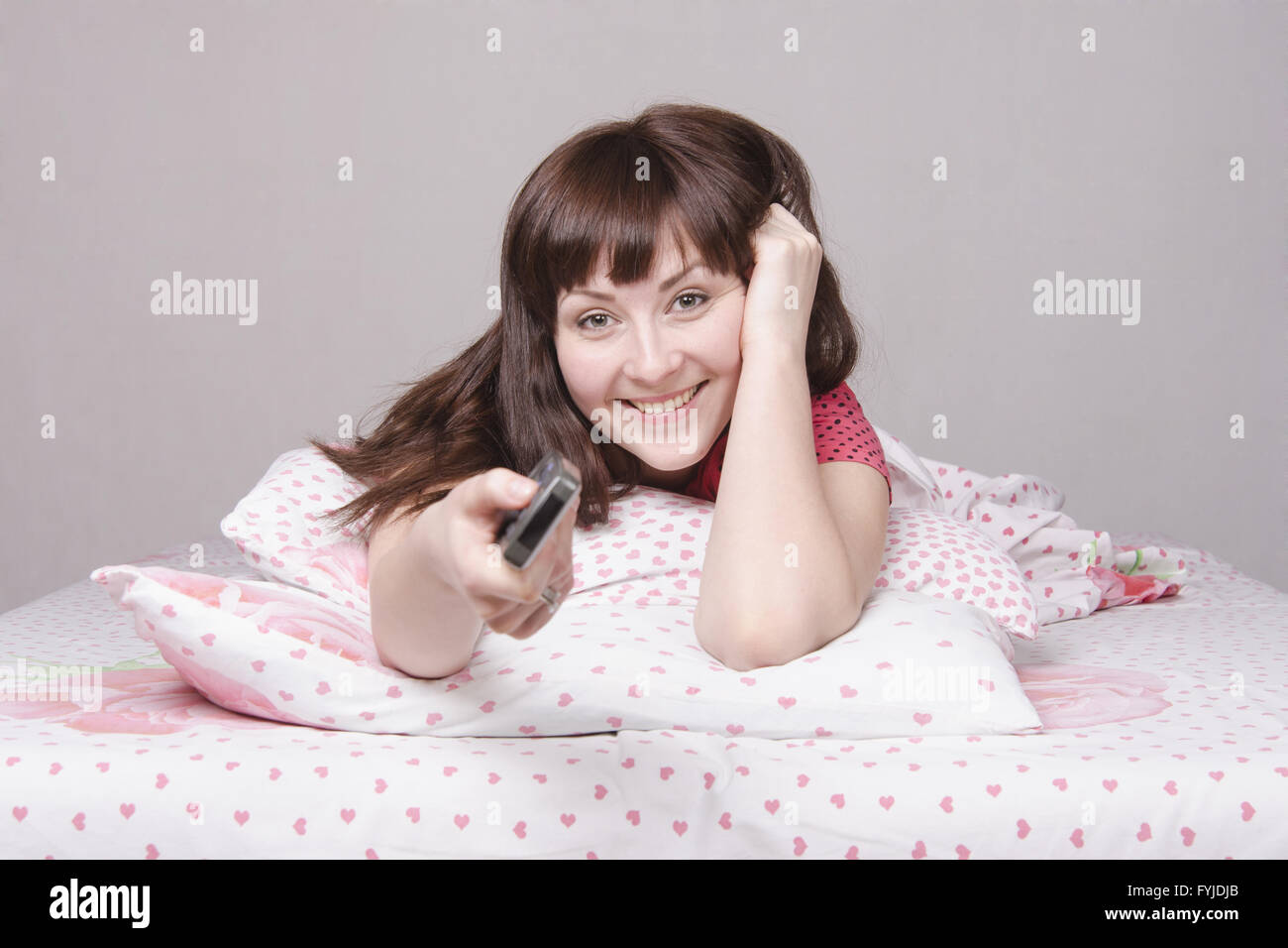 Happy girl with the remote in bed watching TV Stock Photo