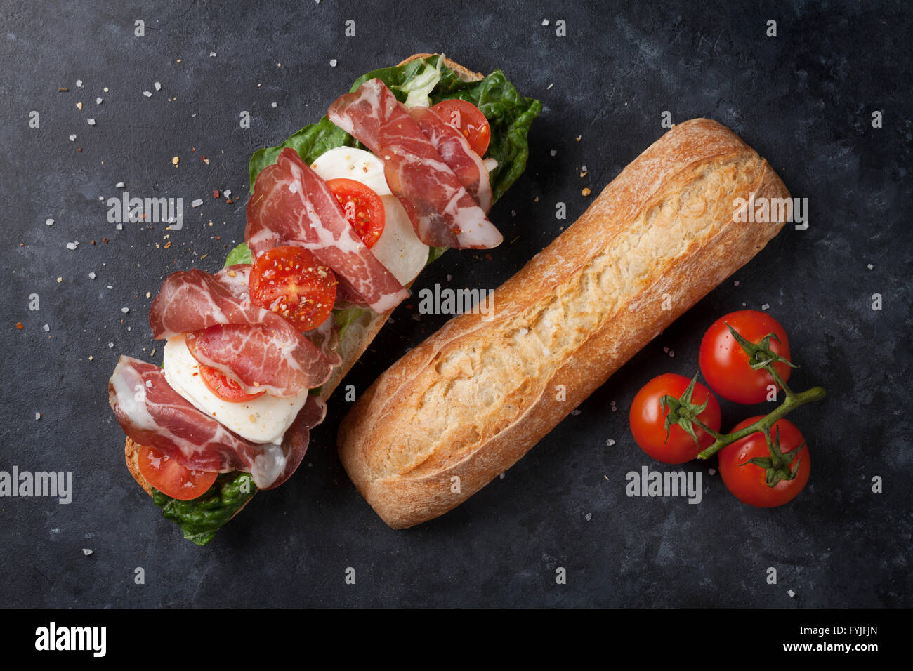 Ciabatta sandwich with romaine salad, prosciutto and mozzarella cheese over stone background