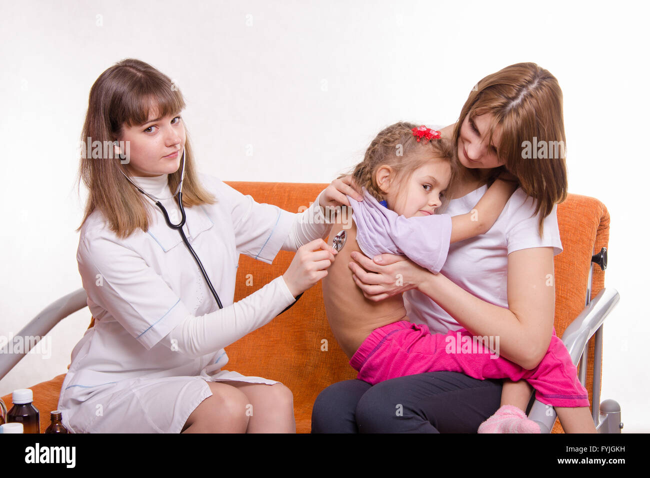 Children's doctor listening to breathing girl sitting in hands of mother Stock Photo