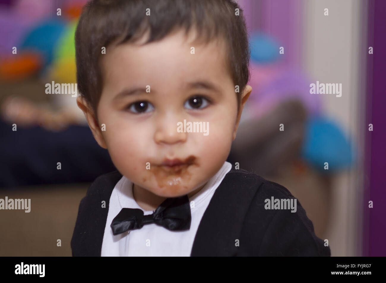 Adorable happy baby eating chocolate, wearing suit and bow tie Stock Photo
