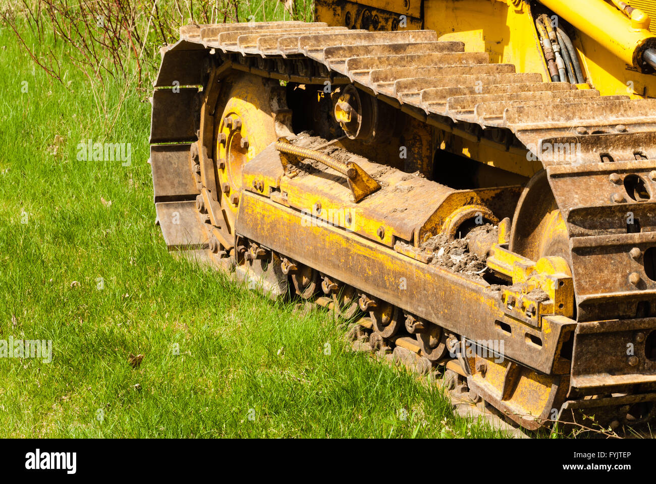 Muddy caterpillar tracks and treads on bulldozer parked on green grass. Stock Photo