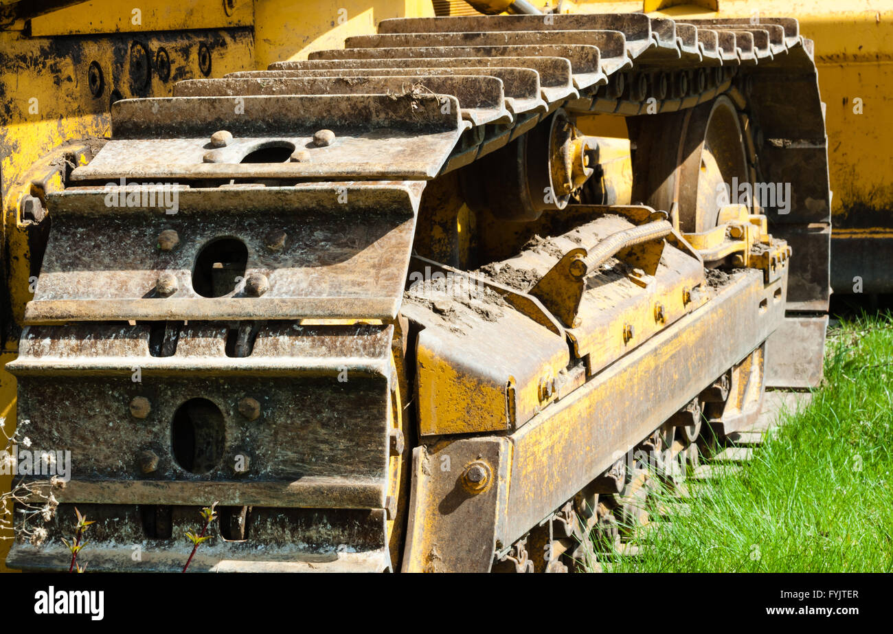 Detail of muddy caterpillar tracks and treads on bulldozer parked on green grass. Stock Photo