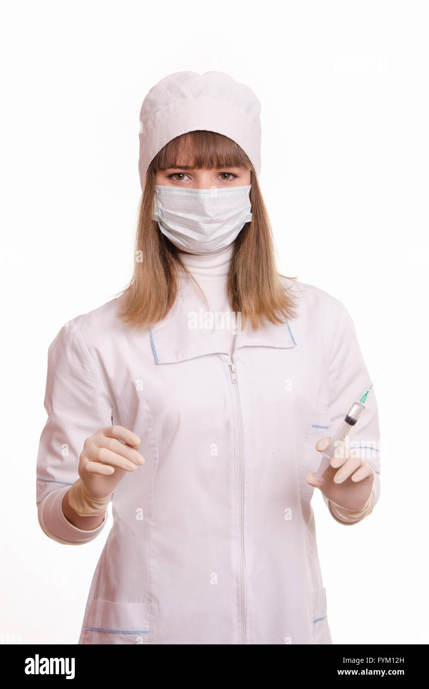 Health worker in a white robe, mask, gloves with a syringe and vial in hands Stock Photo