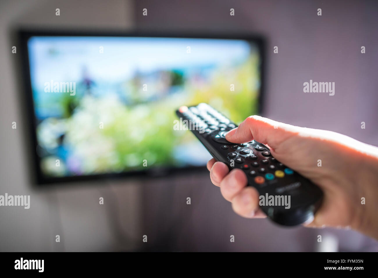 TV and remote control. Hand hold remote. Stock Photo