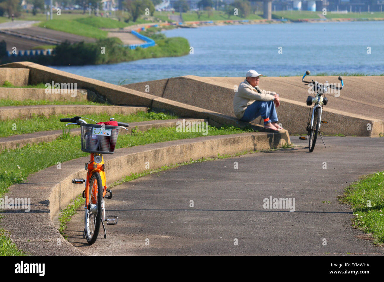 Youbike bicycle parked in the Taipei River park, with man enjoying the sun in the background Stock Photo