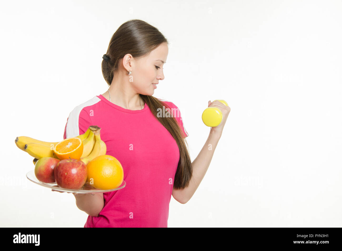 Girl athlete dumbbell raises his hand and other holding a fruit Stock Photo