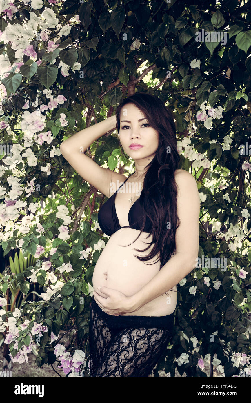 Beautiful pregnant Asian woman amongst flowers Stock Photo