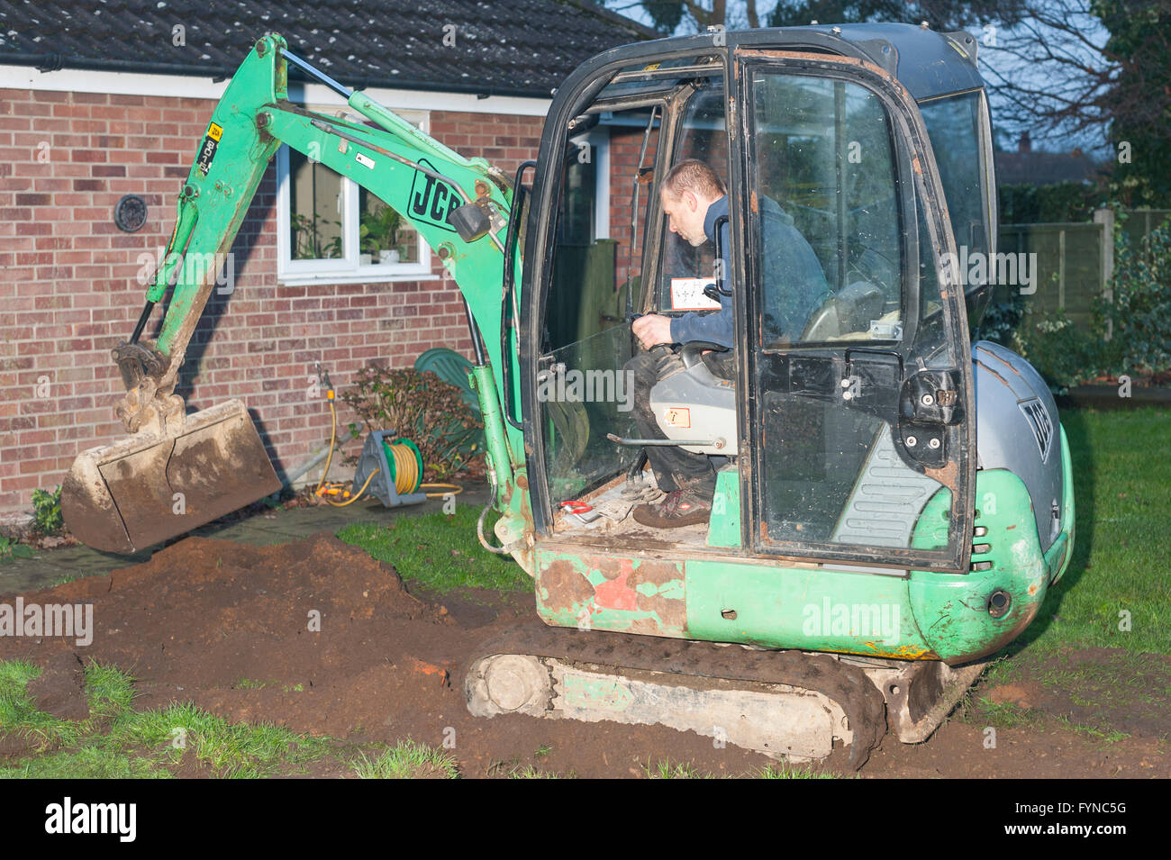 A man in his mini digger filling in a trench in the Uk Stock Photo