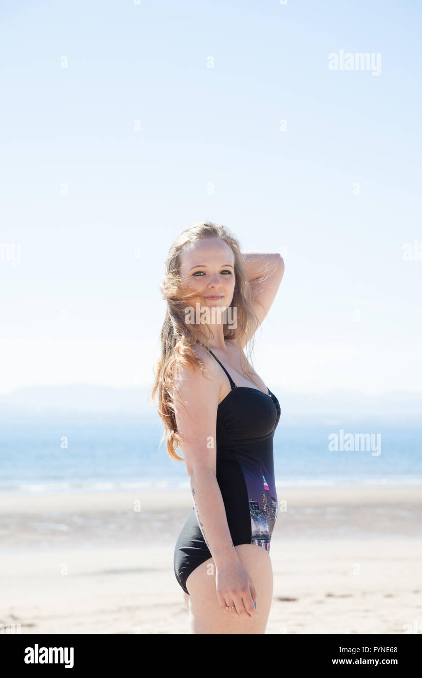 A young woman standing on a UK beach wearing a one piece swimsuit. Stock Photo