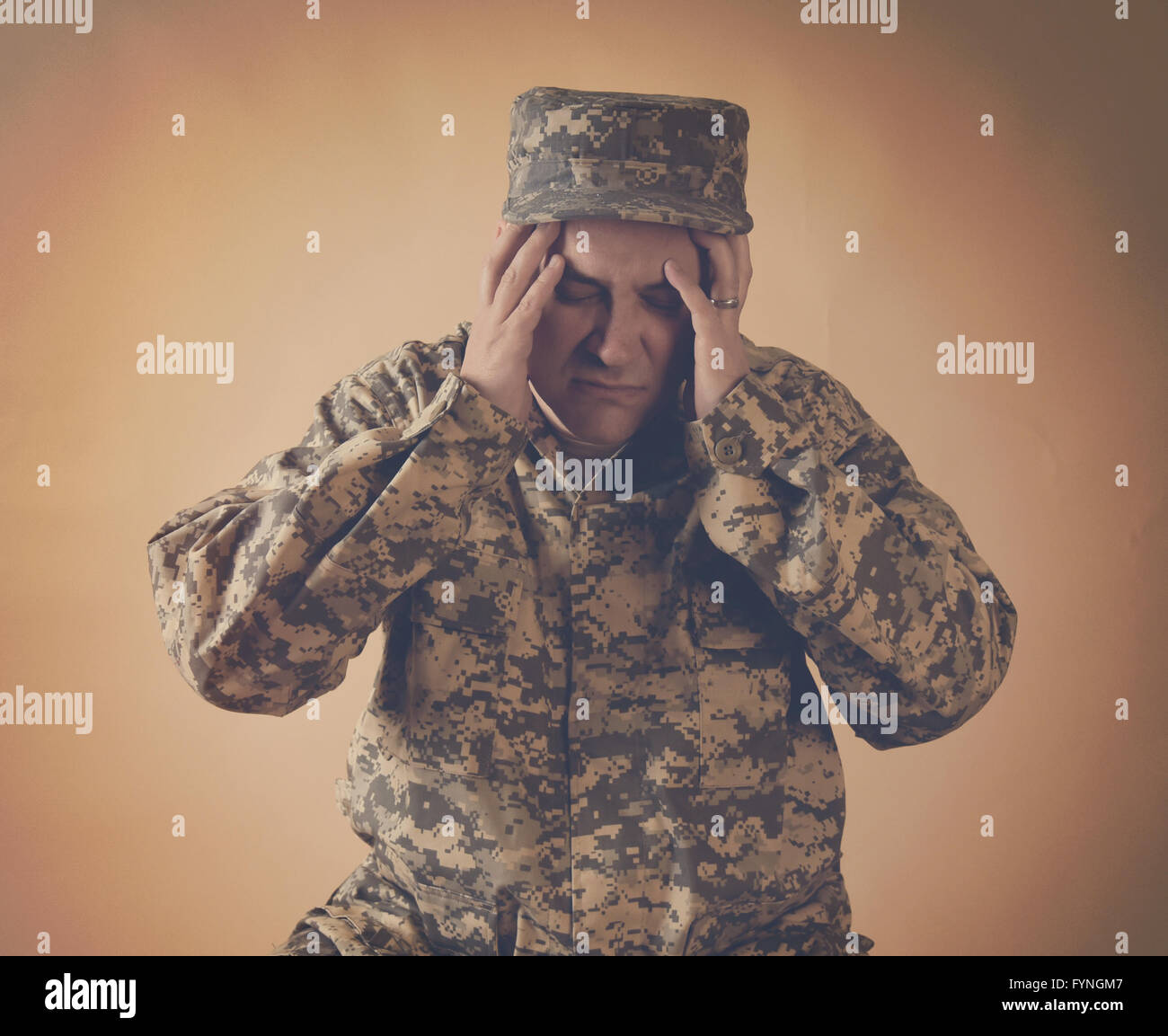 A stressed army man is holding his hands to his head on an  isolated background for a war effect or pain concept Stock Photo