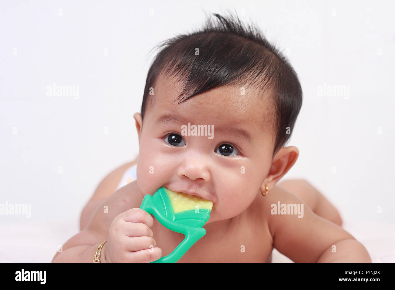 Portrait of cute little Asian baby girl lying down on bed and biting rubber toy Stock Photo