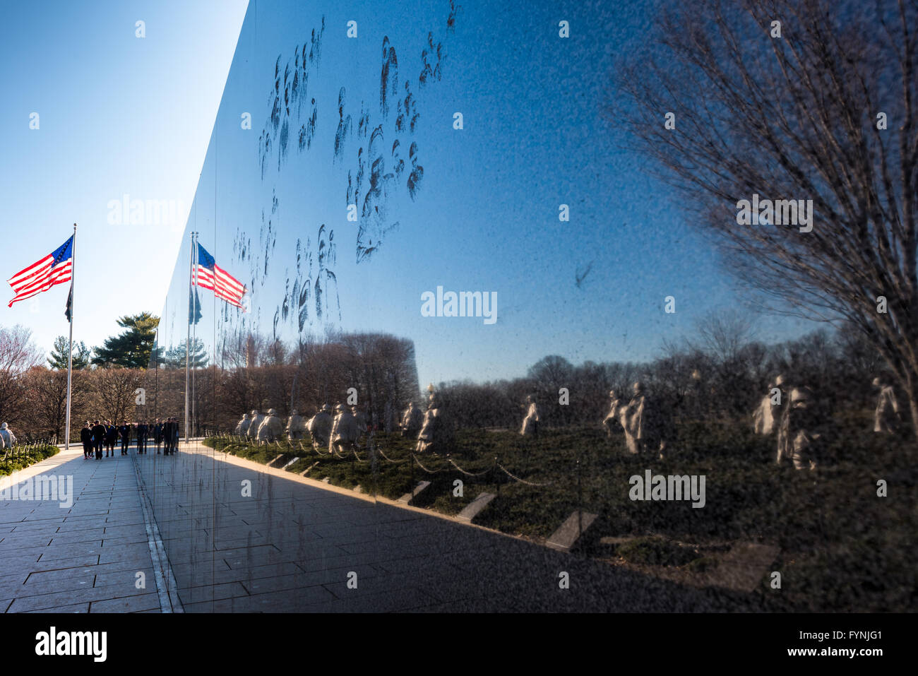 WASHINGTON DC, United States — The black granite Mural Wall reflects the 19 stainless steel statues at the Korean War Veterans Memorial on the National Mall. The wall, etched with more than 2,500 photographs from the Korean War, stretches 164 feet along the memorial site. The reflective surface creates a mirror image of the patrol statues, symbolically representing 38 soldiers. Stock Photo