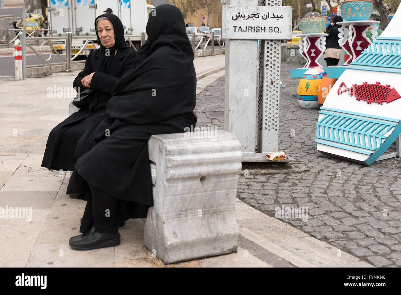 Iranian women wearing black chadors sit on a bench at Tajrish Square in Tehran, Iran. Stock Photo