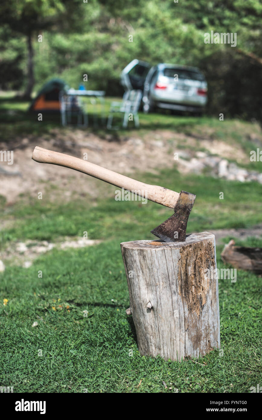 Ax stuck on a stump in the forest. Tent and car on background Stock Photo