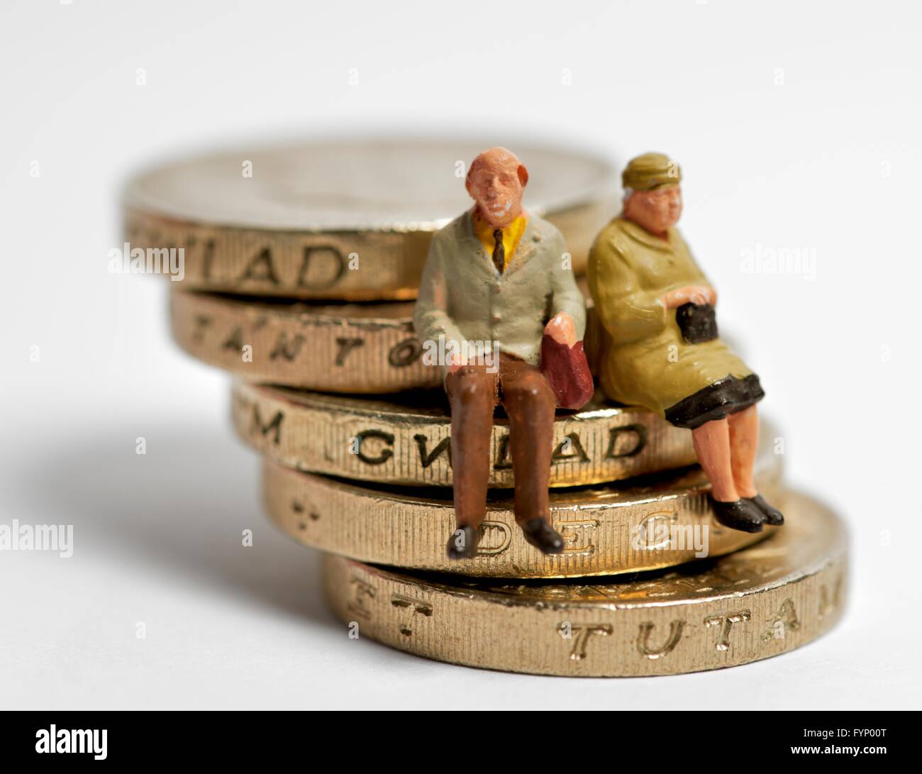Two miniature figurine pensioners sitting on a leaning stack of british one pound coins Stock Photo