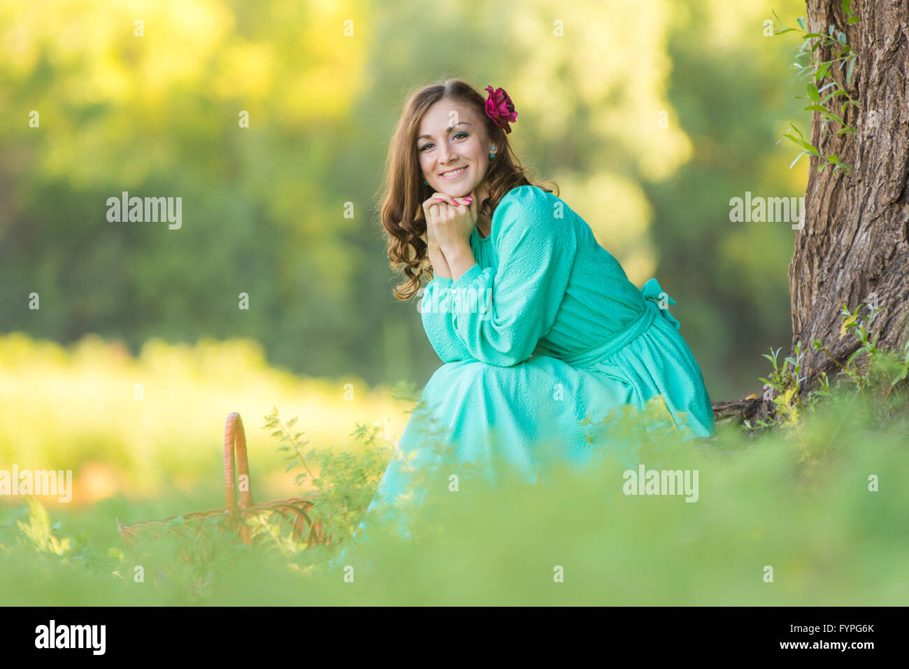 A girl in a long dress smiling while sitting against a tree in the ...
