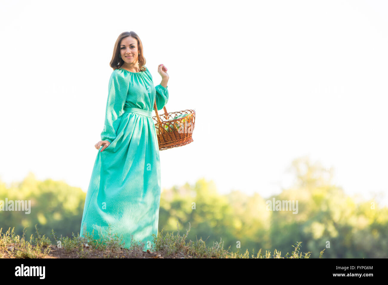 The girl with a basket in a long dress standing on the hill Stock Photo