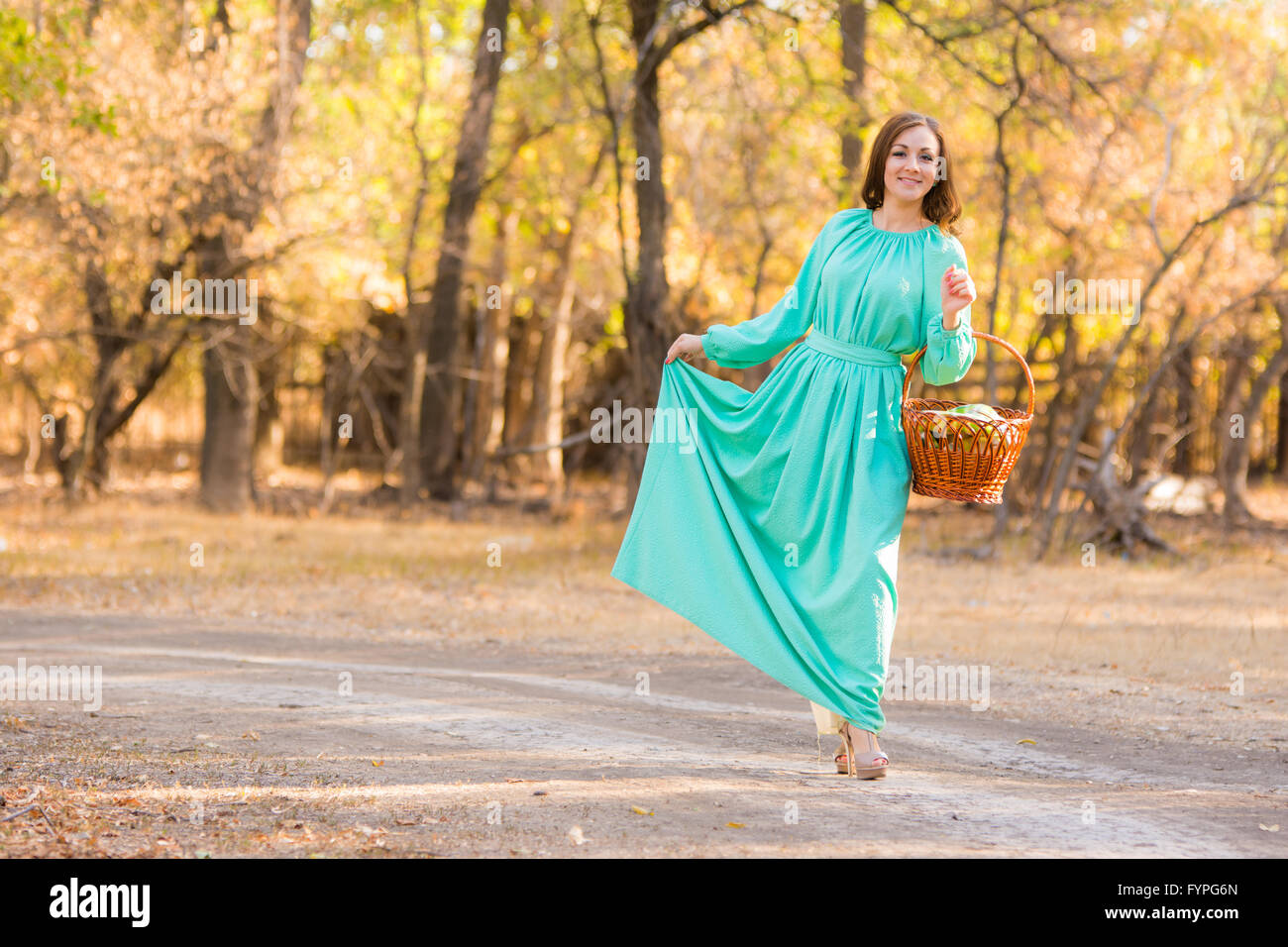 A girl in a long dress holding her dress and a basket of walking on the road Stock Photo