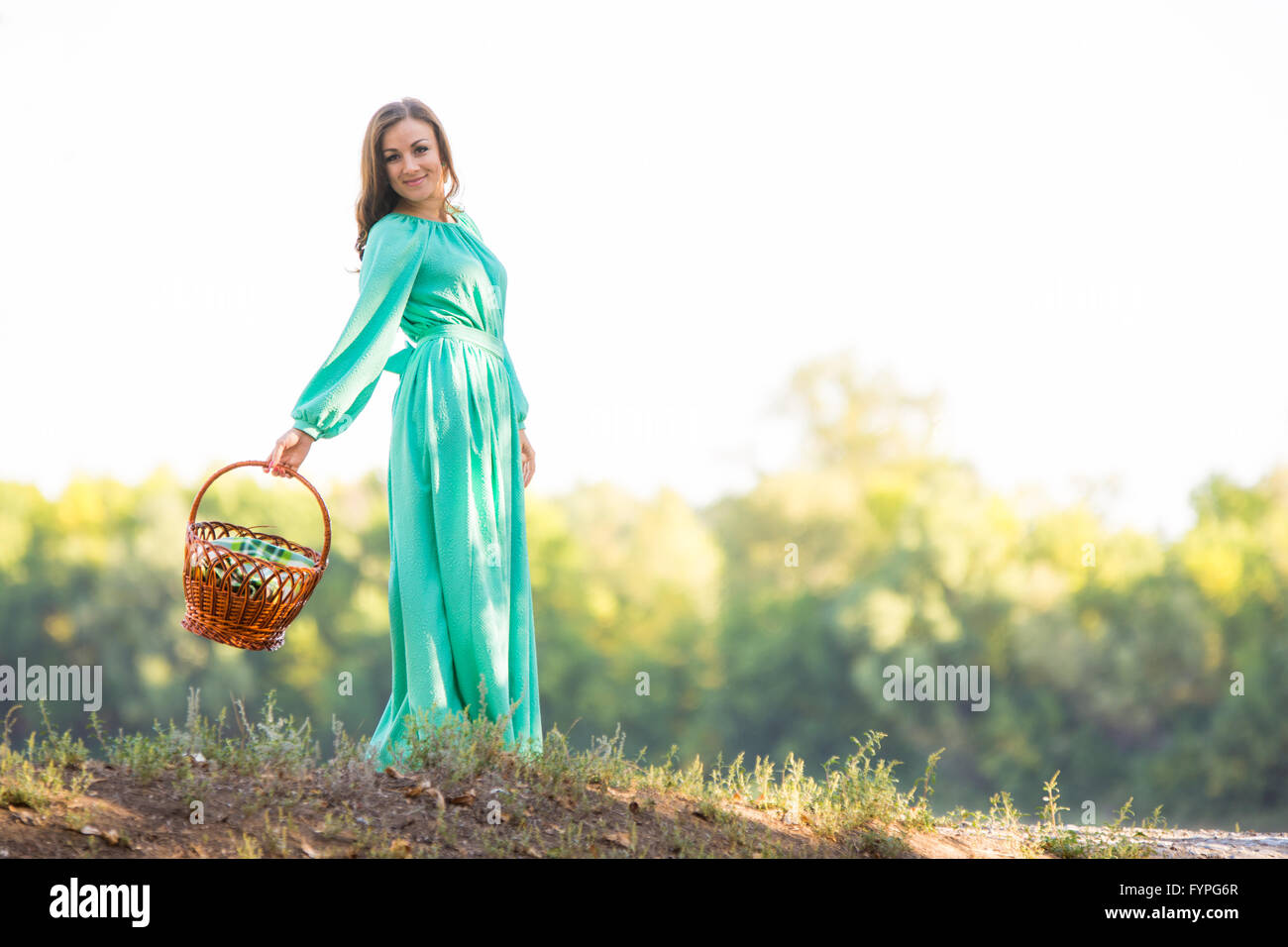 The girl with a basket in a long dress and in a good mood is on the hill Stock Photo