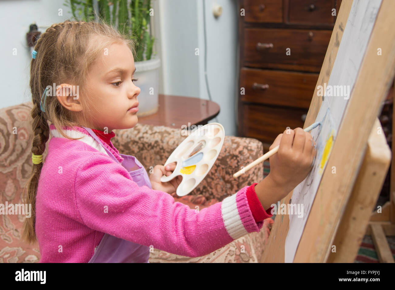 The girl draws a picture paints on an easel in the studio of the artist ...