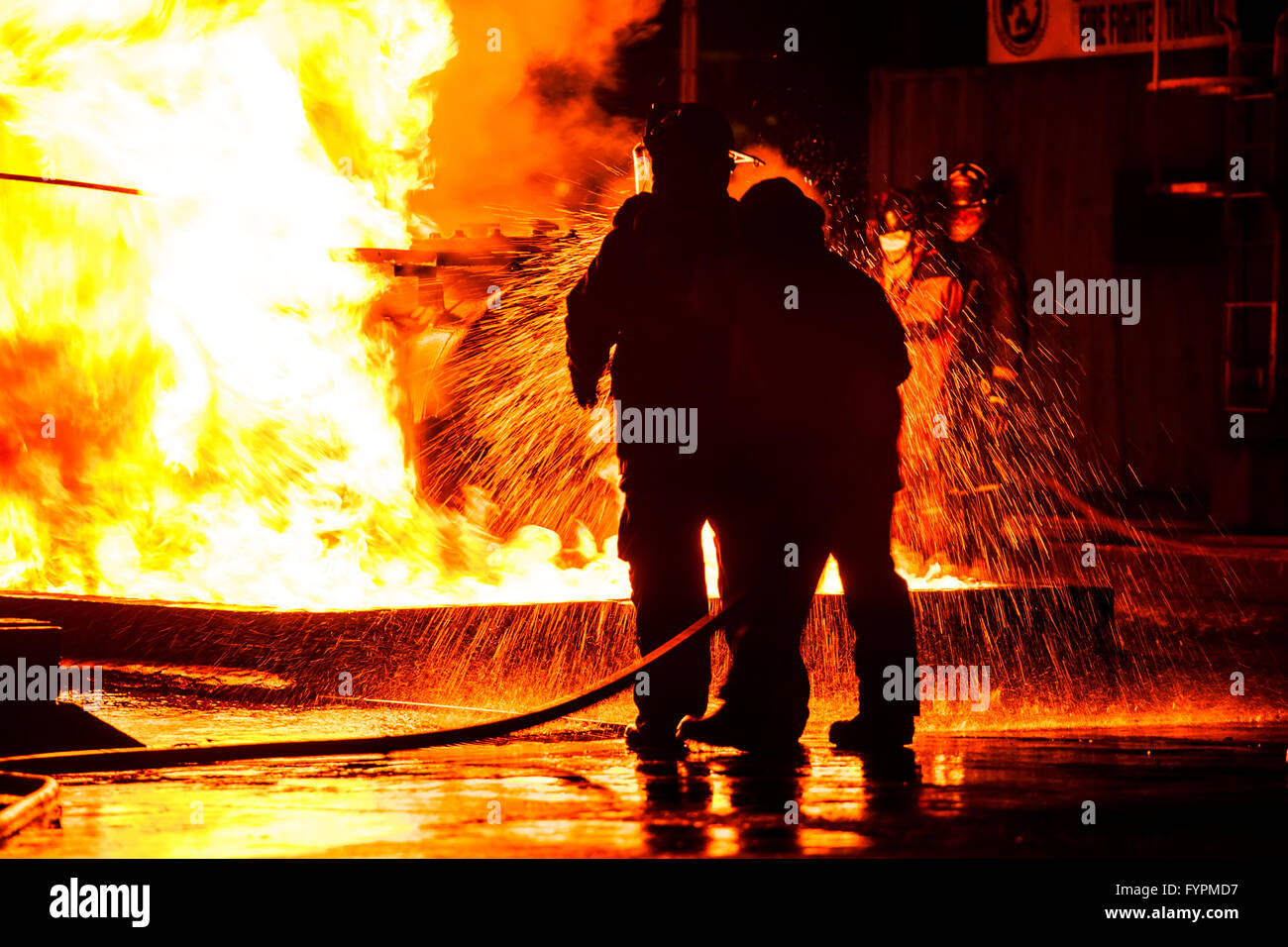Firemen using water hose on raging fire Stock Photo