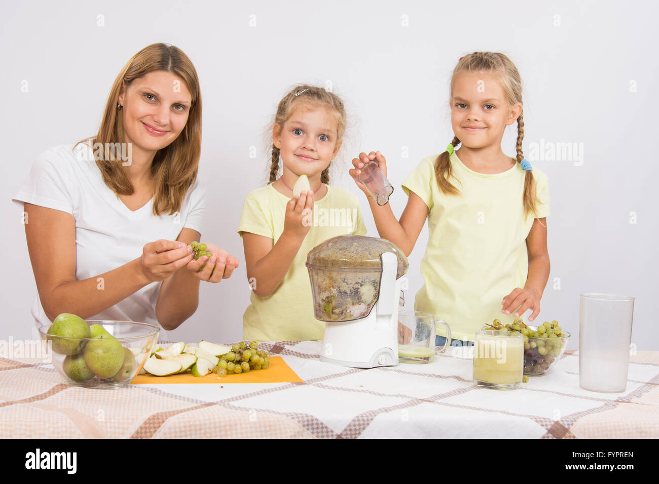 Mother and daughter squeezing juice from pears and grapes Stock Photo