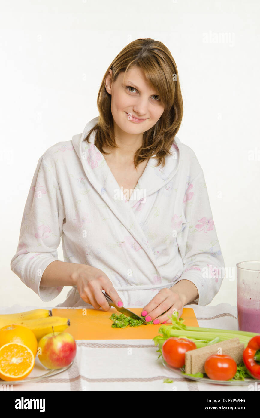 Housewife sitting at the table and cuts the greens for salad Stock Photo