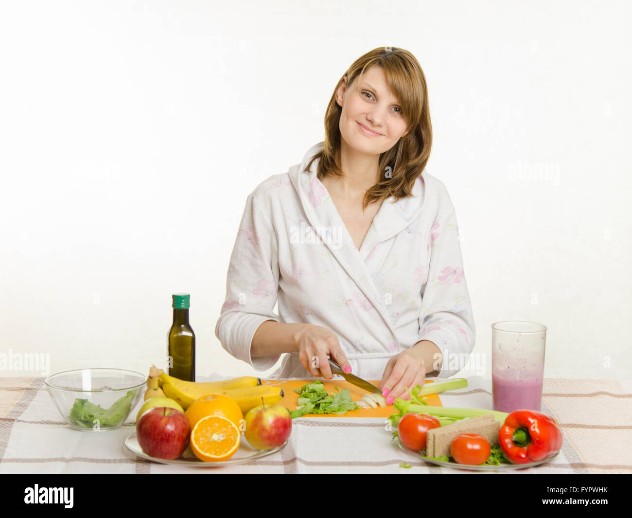 Happy housewife sitting at the table and cut the celery salad Stock Photo