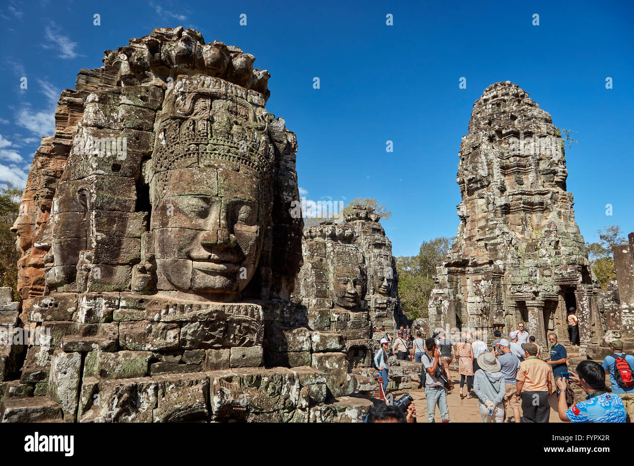 Faces and tourists, Bayon temple ruins, Angkor Thom (12th century temple) Angkor World Heritage Site, Siem Reap, Cambodia Stock Photo