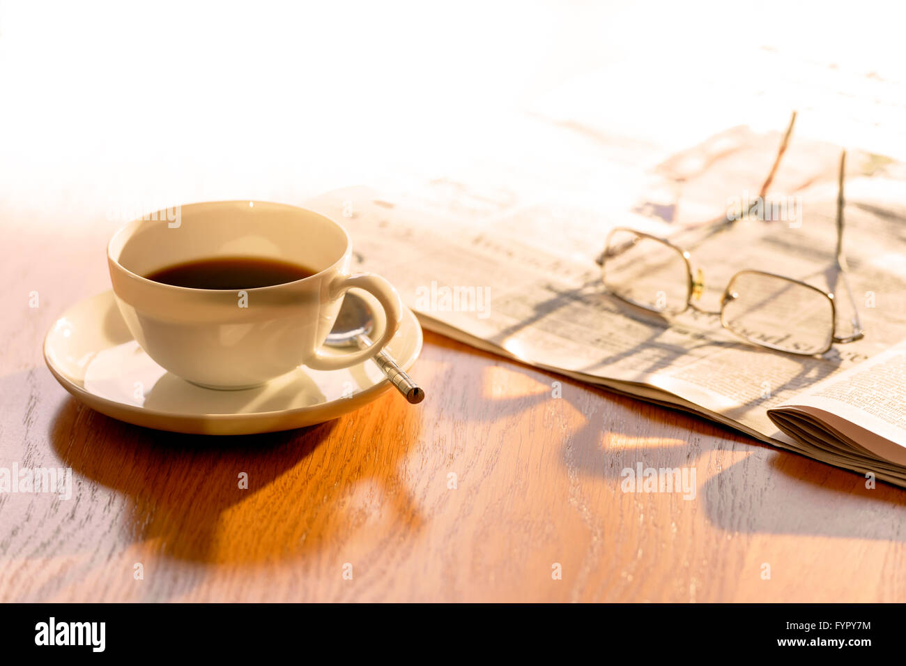 Cup of coffee, with newspaper and glasses, on a bright sunny morning. Stock Photo