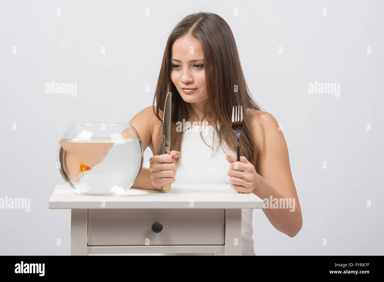Girl holding knife and fork in hand and with an appetite for looking at the little goldfish Stock Photo